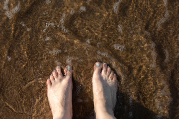 women's feet on the beach in the water coastline warm summer day, rest on the sea