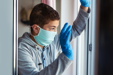 School age boy in a surgeon protection mask sitting by the window . Patient isolated to prevent...