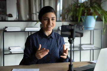 Smiling indian ethnic girl sitting in front of smartphone on stabilizer, recording...