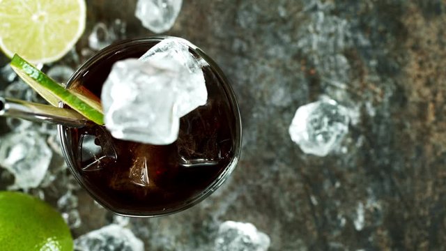Refreshing Cuba libre cocktail in a glass on black stone table, macro super slow motion filmed on high speed cinematic camera.