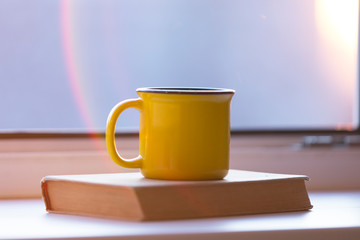 Yellow mug on the book, windowsill, sunset
