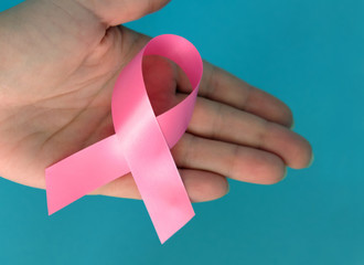 Pink ribbon on a woman's handon and blue background. Breast cancer concept symbolic tape