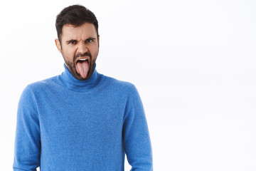 Obraz premium Portrait of disgusted and displeased grimacing funny bearded man, showing tongue and frowning bothered, see something awful, taste bad cooked food, standing disappointed white background