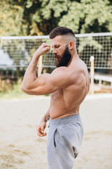 Handsome bearded bodybuilder man with perfect muscular body posing outdoors. Strong man with naked torso standing, looking away.