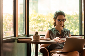 Beautiful caucacsian woman wear glasses use internet via laptop in cafe during morning and have a cup of coffee