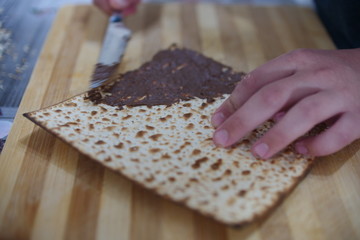 A child's hands are spread chocolate on matzah. Matzah - a traditional Jewish food for Passover.