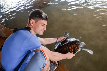 Young brunette guy with camera releases turtle into water, volunteer saves turtles, animal protection, boy takes pictures of turtle. saving animals  Sea Conservation Research Project  Center in Bentot