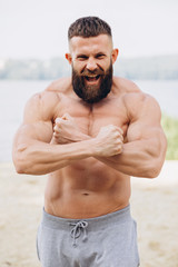 Brutal bearded bodybuilder man with perfect muscular body posing outdoors near lake. Strong man...