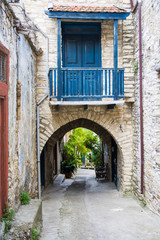 Fototapeta na wymiar Cyprus village Lefkara. View of a village stony street decorated by green bushes. Street go through an arch with balcony with a blue wooden door.