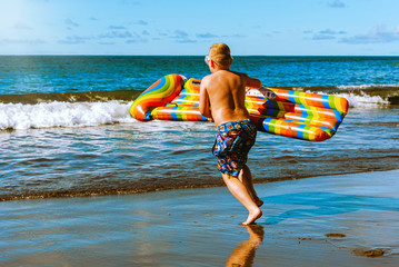Beach vacation. A boy with an air mattress runs into the sea