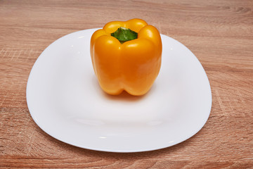 Colorful yellow bell peppers in a white plate on wooden table. Top view with copy space. flat lay