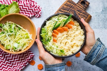 Couscous wheat durum millet tabbouleh in bowl with greens and vegetables in woman hands.