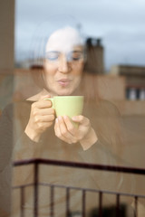 woman with hot cup of infusion at home looking out the window