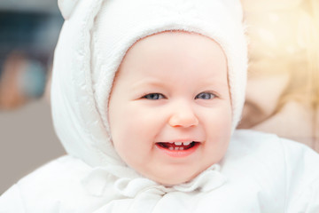 Portrait of a cute smiling Caucasian baby girl outside. Child toddler in white warm clothes walking outdoor. Laughing funny lovely young kid with blue eyes. Happy childhood lifestyle.