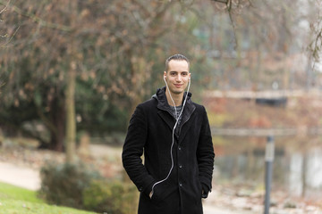 Man Wearing Black Coat and Listening to Earphones in Urban Park