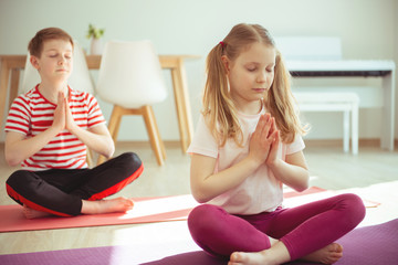 Cute teenager children making yoga at home during coronavirus quarantine