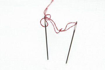 Obraz premium On a white background two sewing needles connected by a red thread. Concept - mutual relations, irritation from self-isolation and quarantine, figurative meaning