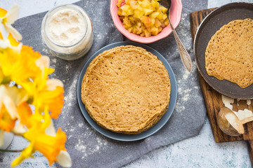 Crepes on plate. Thin pancakes and apples for filling. Sweet vegan dessert. Ingredients on table in kitchen. Vegan food