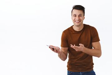 Technology, people and communication concept. Happy laughing guy in brown t-shirt, smiling with satisfied grin, holding mobile phone, pointing at smartphone as impressed with awesome new app