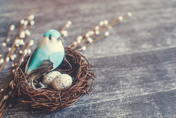 Easter background. Nest with easter eggs and decorative blue bird on wooden background. Selective...