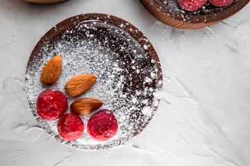 Appetizing tart with dark chocolate, raspberries, almond and powdered sugar. Natural light and color grade, top view, flat lay. White colored textured background. Copy space  