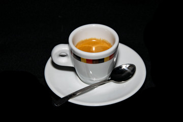 a cup of freshly grounded espresso coffee alongside a plate and spoon 