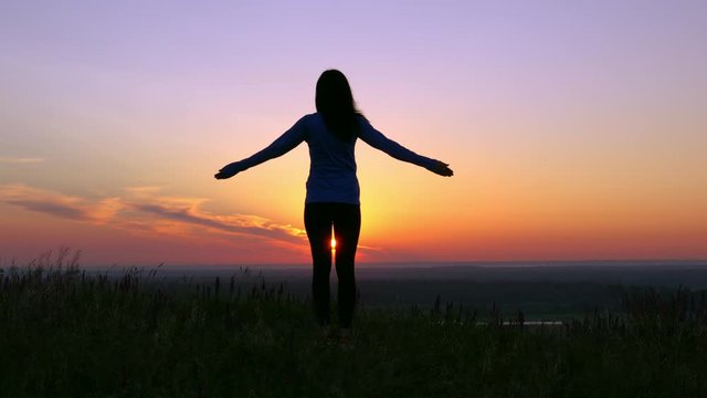 back view silhouette woman standing on the hill doing yoga meditation at sunrise rising sun at countryside
