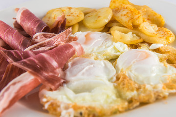 Plate of broken eggs with ham and potatoes.