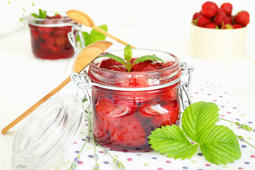 Delicious strawberry jam in traditional glass jar on white wooden background