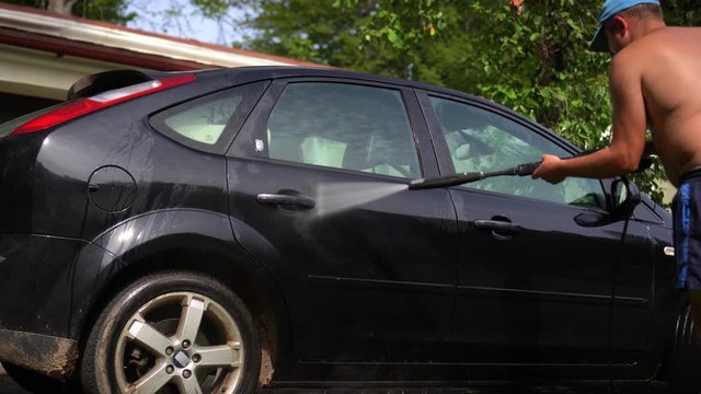 Bald man worker with big nude belly washes car using high pressure water jet