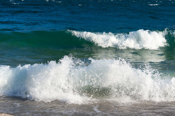 During windy days, the water of Lake Garda reaches the shore forming frothy and shiny waves that break and stretch on the pebble beach. In autumn the water has a very dark blue color. Italy.