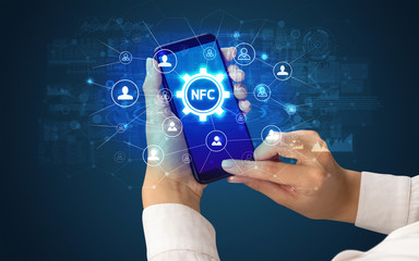 Female hand holding smartphone with NFC abbreviation, modern technology concept