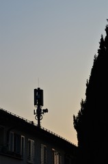 Mobile antenna as a silhouette on a house roof with a blue sky