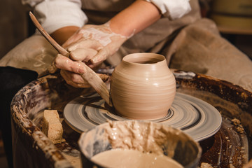 woman in an apron creates a vase from clay on a potter's wheel