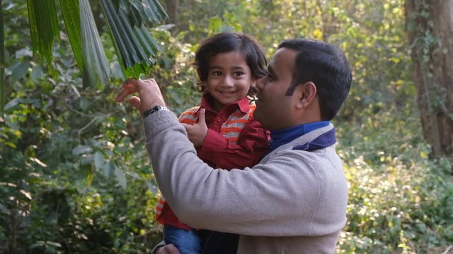 An Indian brunette father and his baby boy in winter garments enjoying themselves in winter afternoon on a  dry grass field in forest background. Indian lifestyle and parenthood.