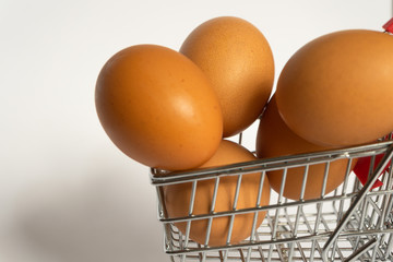 Toy little consumer food trolley from steel with red plastic handle on a gray background with five fresh egg inside. empty space