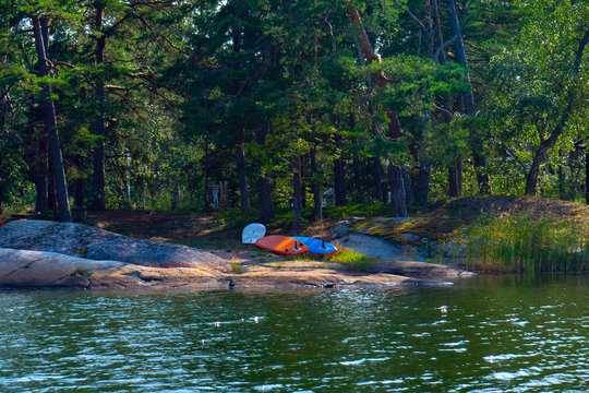 Three Tandem Canoe Upside Down On A Rocky Shore.