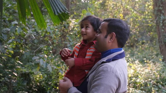An Indian brunette father and his baby boy in winter garments enjoying themselves in winter afternoon on a  dry grass field in forest background. Indian lifestyle and parenthood.