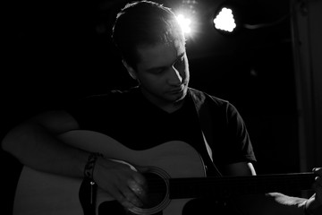 A young handsome guy of European appearance plays an acoustic guitar and sits on a chair. Black and white photography.