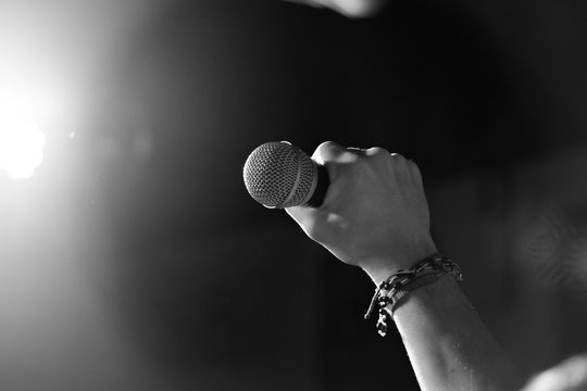 Male hand raised up with bracelets in his hands holds a microphone. Back and white photography