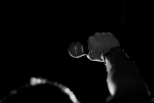 Male hand raised up with bracelets in his hands holds a microphone. Back and white photography
