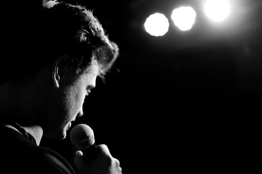 Young handsome guy emotionally sings and speaks into the microphone. Black and white photography