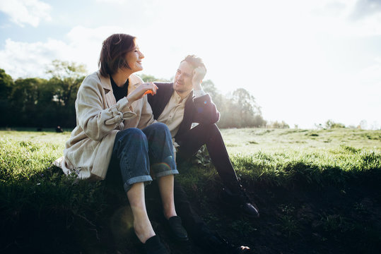 Loving hipster couple walking in the field, kissing and holding hands, hugging, lying in the grass in the spring at sunset. Photo with lens flare