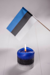 burning candle in national estonia colours in front of estonian flag 