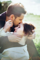 Fototapeta premium Loving hipster couple walking in the field, kissing and holding hands, hugging, lying in the grass in the spring at sunset. Photo with lens flare