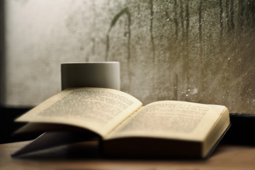Open book with mug cup, rainy window