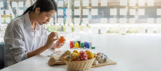 Happy Asian woman painting eggs for Eastertime at home. Family preparing for Easter.