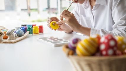 Happy Asian woman painting eggs for Eastertime at home. Family preparing for Easter.