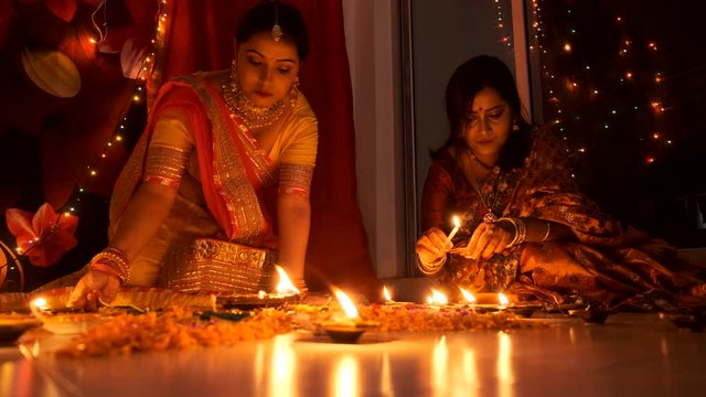 Two beautiful Indian Bengali women in Indian traditional dress lightening diyas/lamps in the floor in light bokeh background on Diwali evening. Indian lifestyle and Diwali celebration