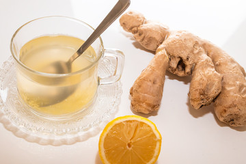 Glass cup of hot ginger tea with ginger rhizome (root) sliced and lemon, isolated on white background.